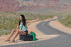 video of a woman waiting for someone to pick her up in the middle of desert. the rolls royce car shows up from the background and stop. a door opens. the woman is smiles, stands up and jump to how her joy.